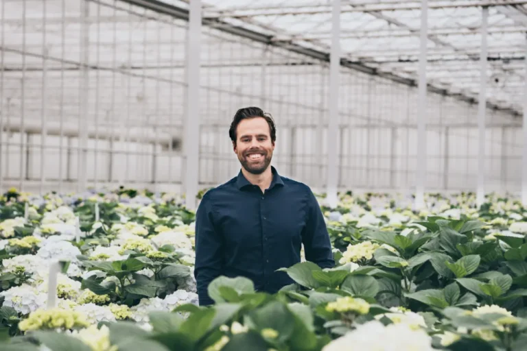 Man in een kas tussen bloeiende hortensia's met een glimlach op zijn gezicht.
